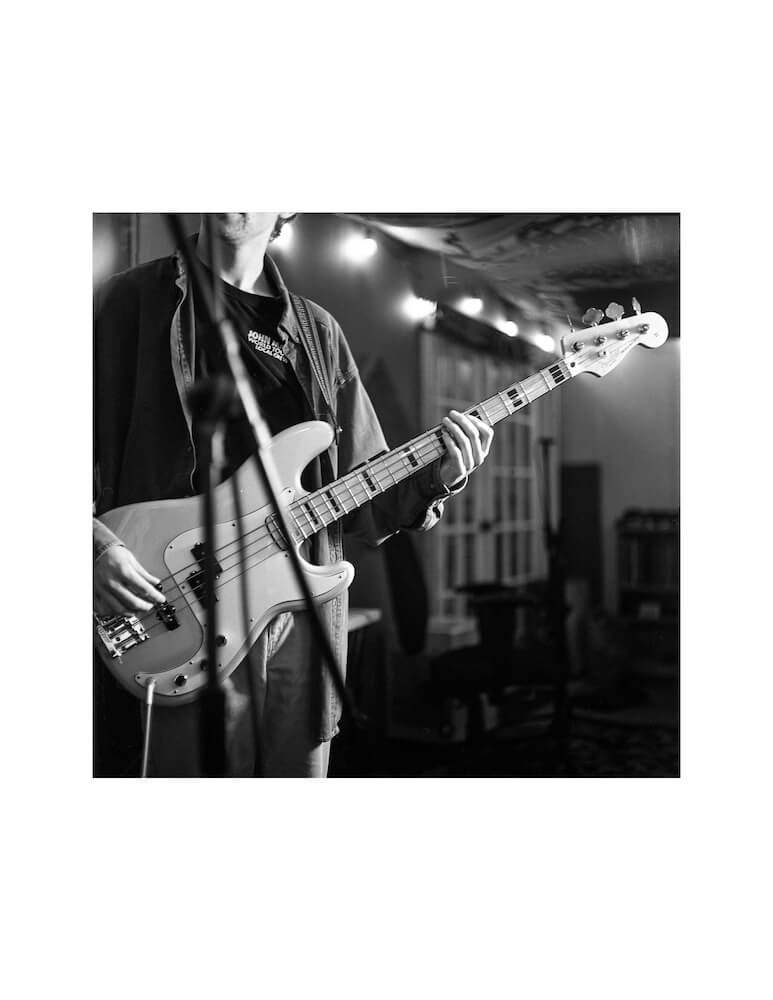 a scan of a medium format film black and white negative of a man from the neck down playing a bass guitar