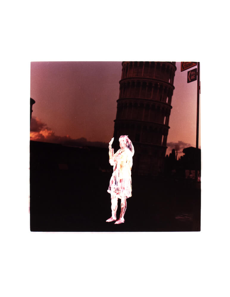 a color film photographic print of an obscured tourist holding up her hand to pretend she is holding up the Leaning Tower of Pisa in Italy