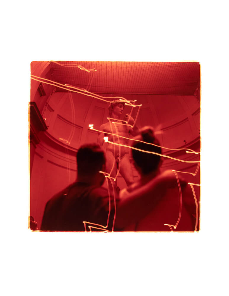 a red medium format film color darkroom fine art print of a couple looking at the statue of David in Florence Italy covered by light trails