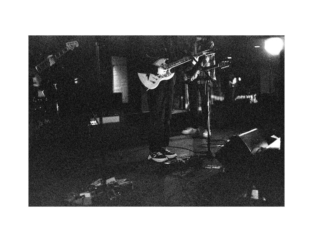 35mm black and white fine art film photograph of a below the neck view of a musician playing a guitar at a concert