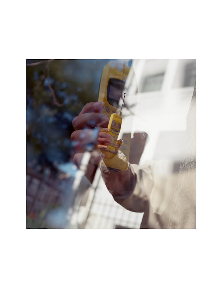 color film fine art photograph with two layered images of a hand holding a yellow cell phone